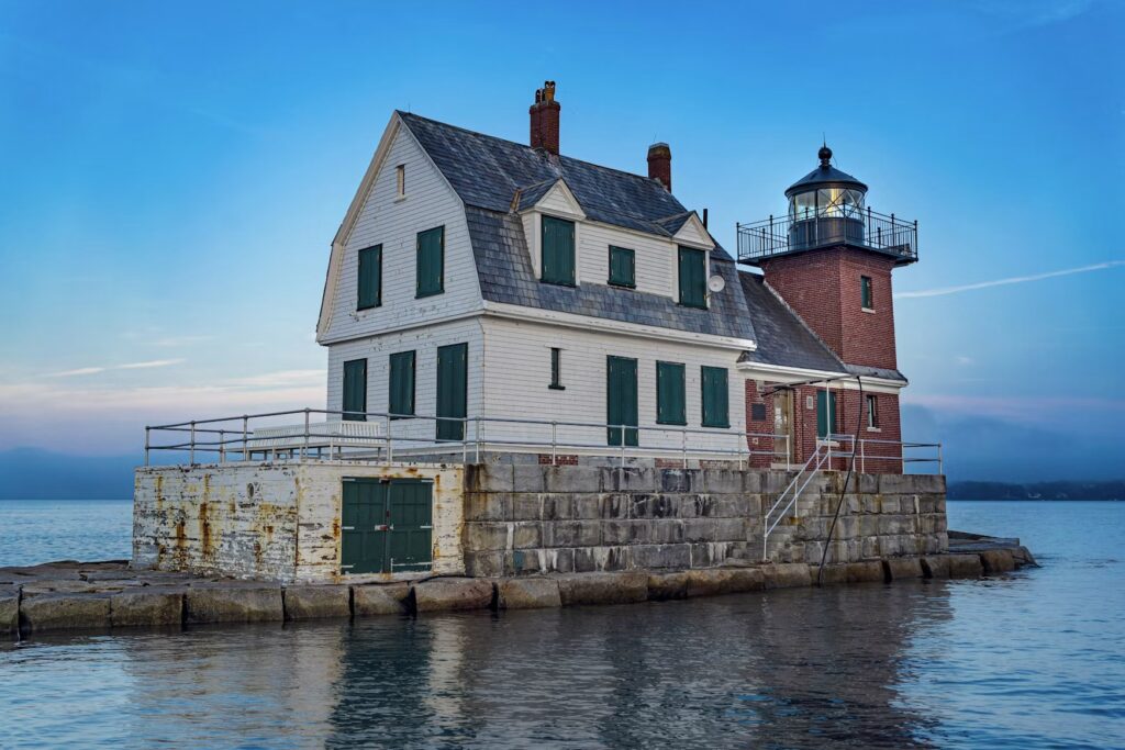 A white building and lighthouse tower sitting at the end of the stone breakwater in Rockland. 