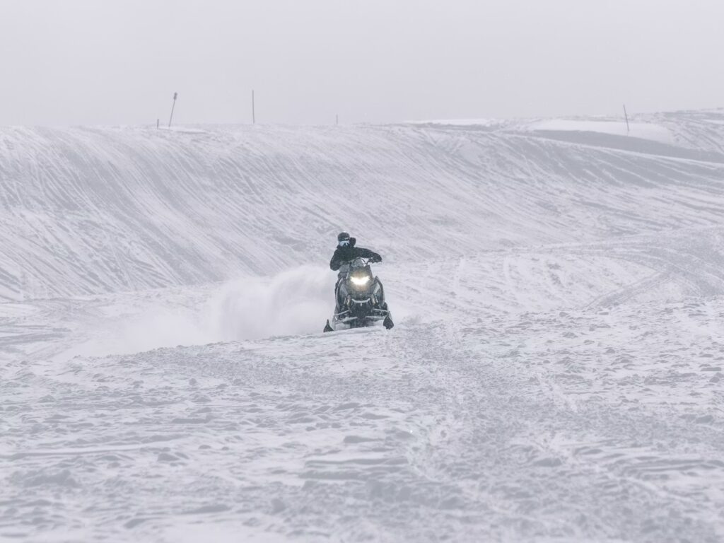 A rider driving a snowmobile through a snowy white winter landscape. 