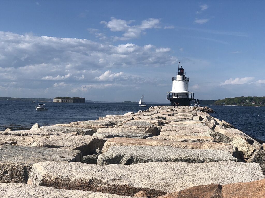 The Spring Point Ledge Lighthouse sitting at the end of a long, uneven granite breakwater in the harbor. 