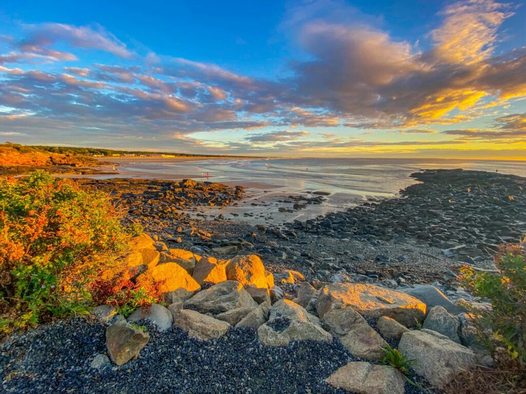 Golden sunlight illuminating a rocky coastal shoreline and calm ocean waters at sunset.