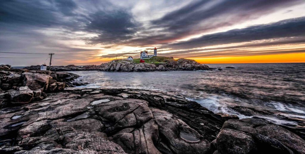 9 Best Things to Do in York, Maine: From Nubble Light to Mount A A stunning sunset view over the rocky coast and Nubble Lighthouse in Cape Neddick, best things to do in York Maine.