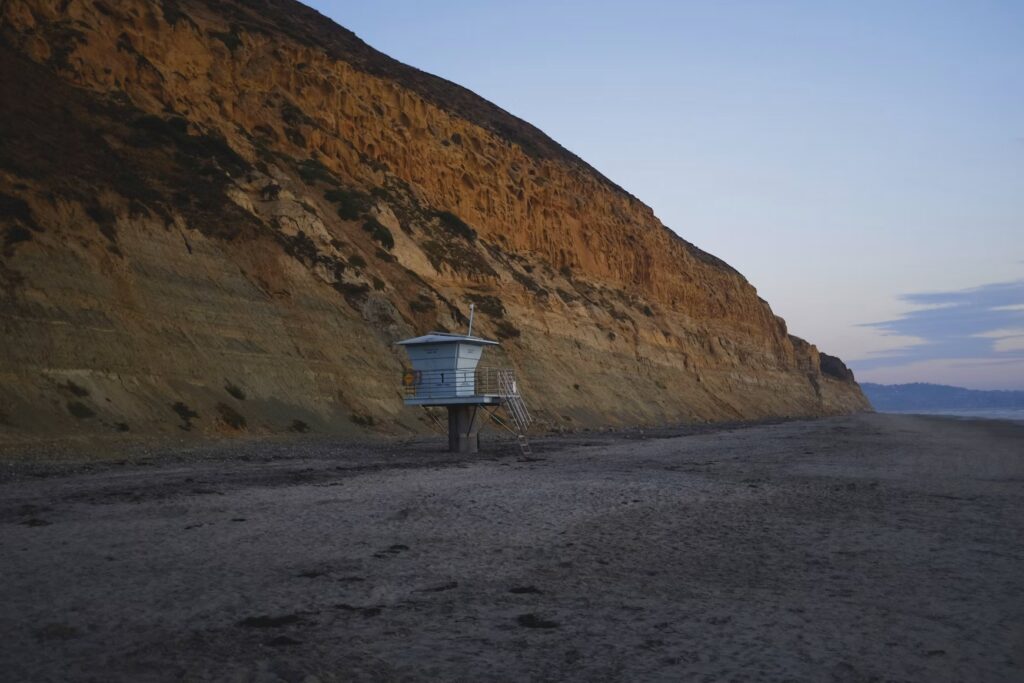 A small lifeguard tower standing beneath the towering sandstone bluffs of Black's Beach.