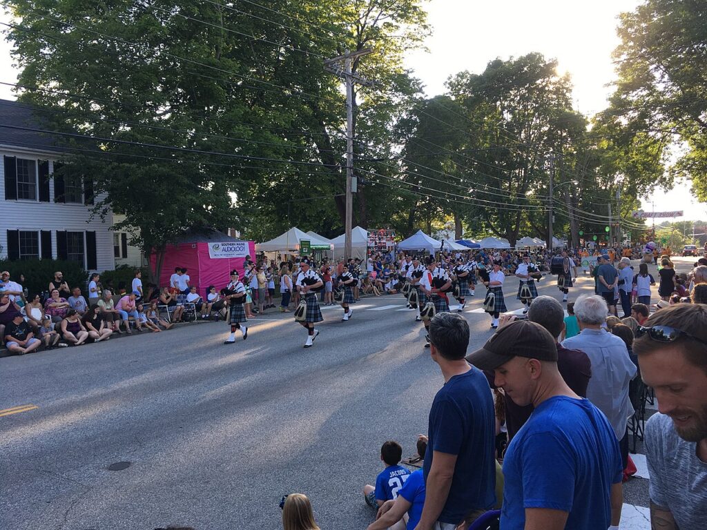 People watching a local summer parade marching down a tree-lined street.