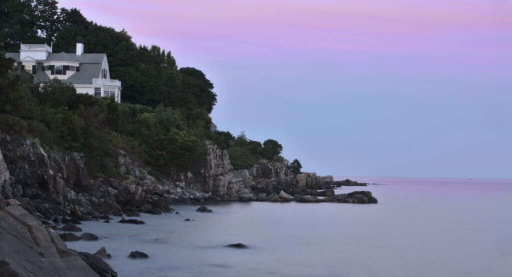A large coastal home perched on steep, rocky cliffs overlooking the ocean along the York Harbor Cliff Walk, Maine.