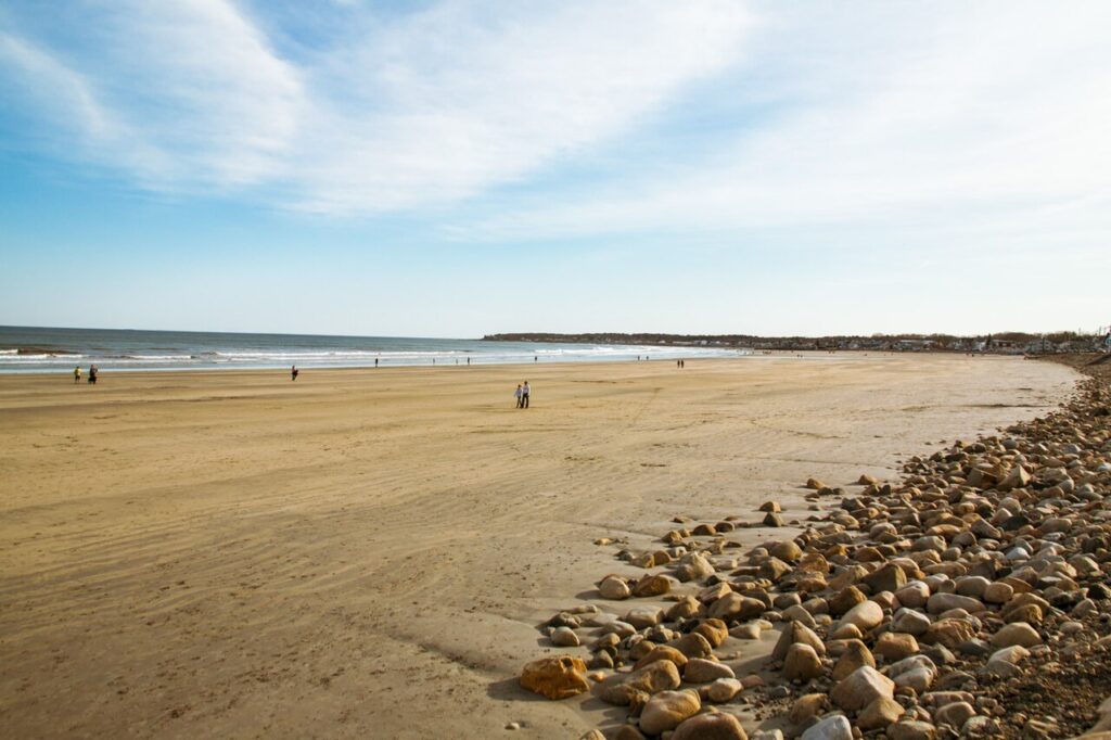 A wide, expansive stretch of smooth sand meeting the ocean with a few rocks in the foreground at a beach in York, Maine.