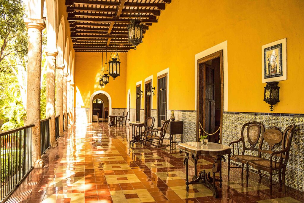 9 Best Hotels in Mexico: Authentic & Boutique Stays (2026) Sunlit corridor of an authentic Mexican boutique hotel featuring yellow walls, arched walkways, and patterned tile floors.