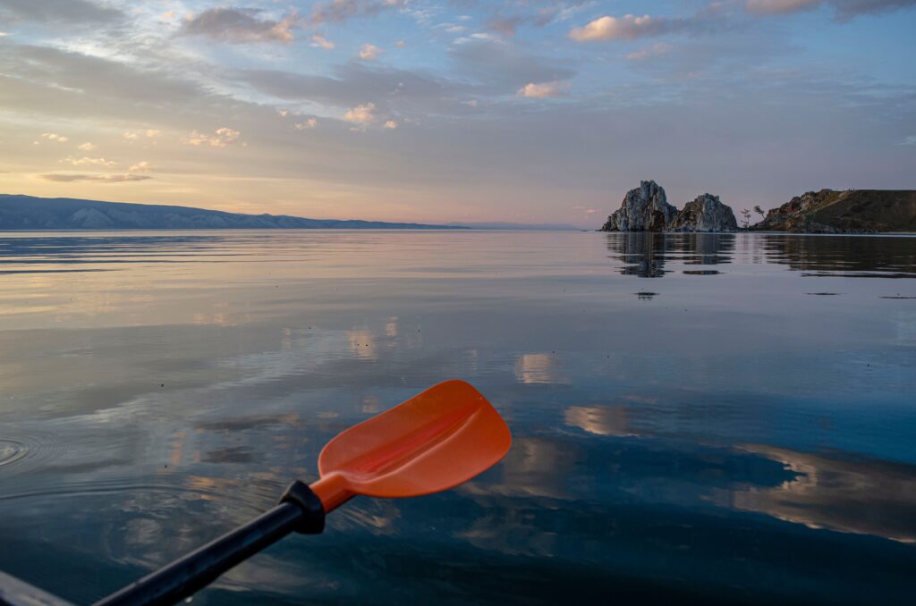 An orange kayak paddle hovering over calm glowing waters.