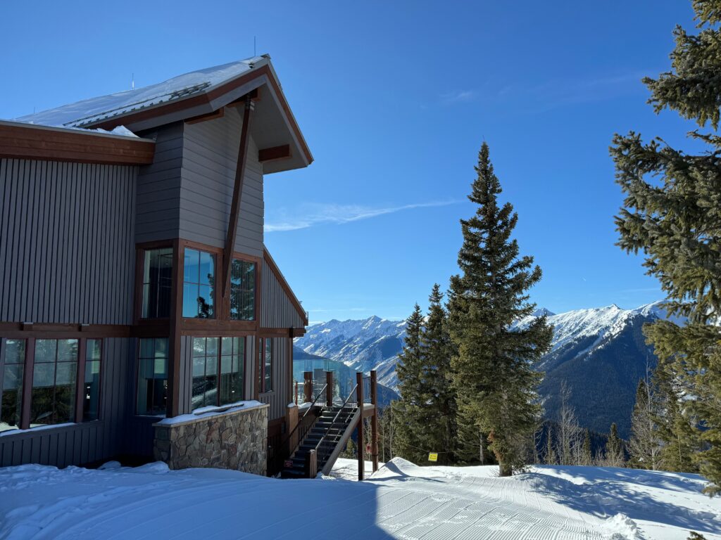 Best Places to Stay in Colorado: 7 Areas & 21 Hotels (2026) Cozy mountain lodge with large windows overlooking a snow-covered landscape and alpine peaks, as one of the best places to stay in Colorado.