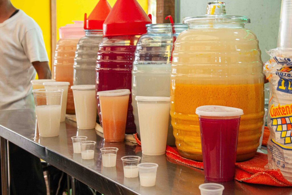 Colorful traditional pulque served in large glass jars on a metal counter at a cantina in Mexico City. 