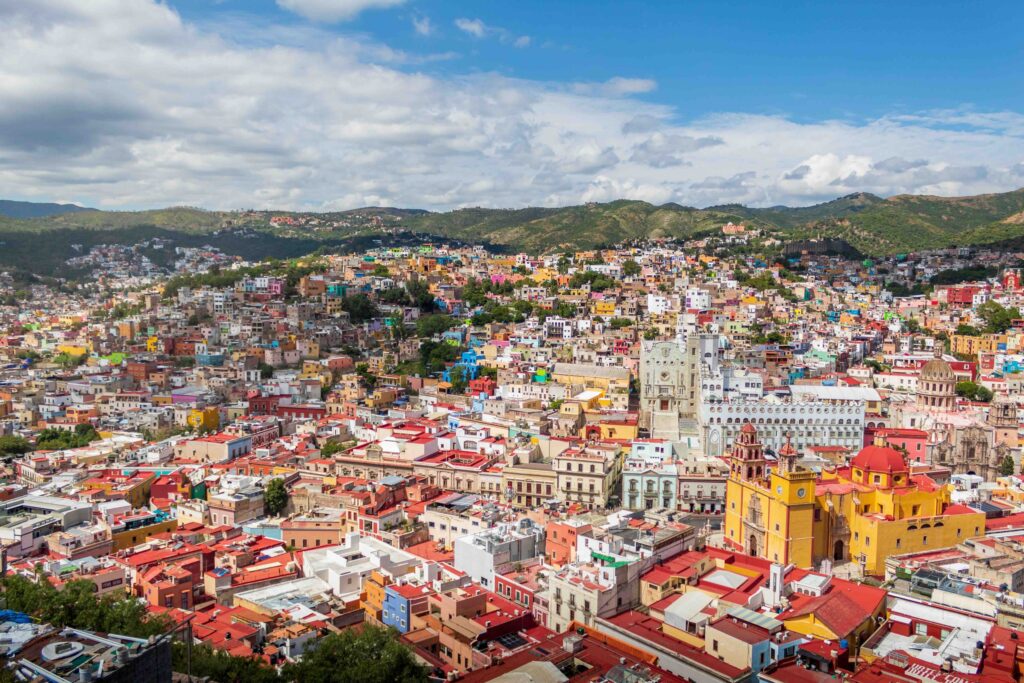 11 Safest Cities in Mexico: A 2026 Worry-Free Guide (+ 3 to Avoid) Colorful hillside houses and yellow Basílica in Guanajuato old town under blue sky, Mexico