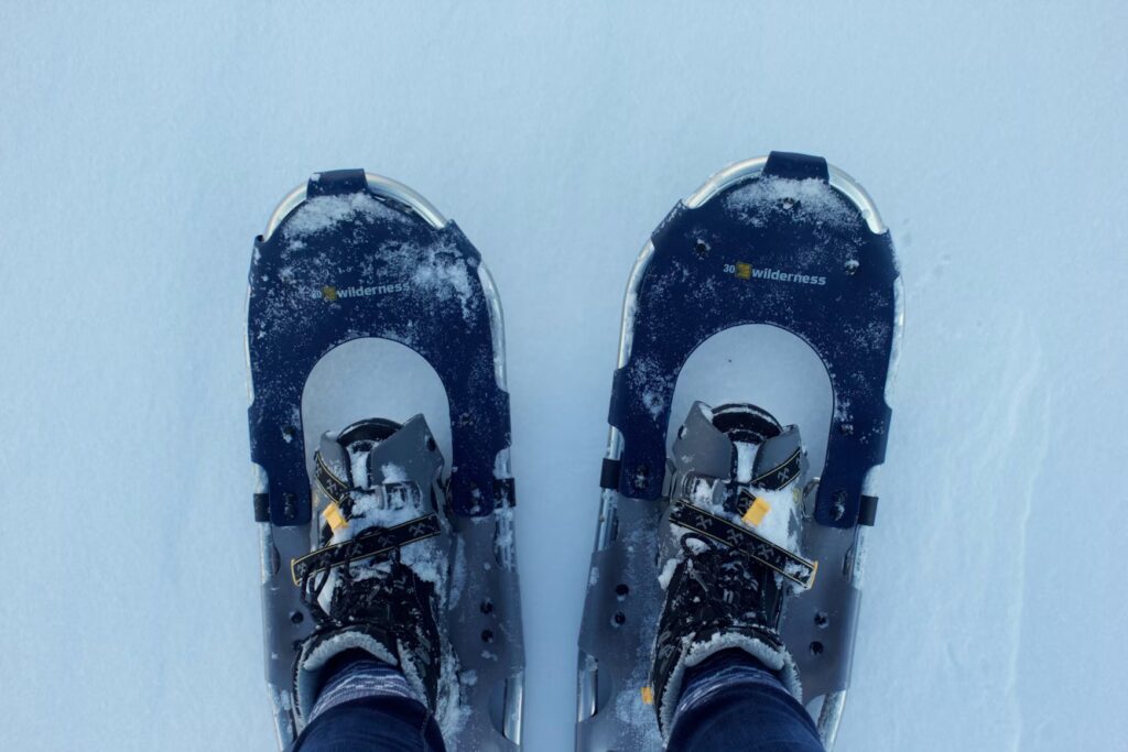 Looking down at a pair of feet wearing snowshoes on white snow. 