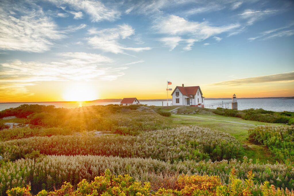 A scenic lighthouse and keeper's house surrounded by coastal vegetation at sunset.