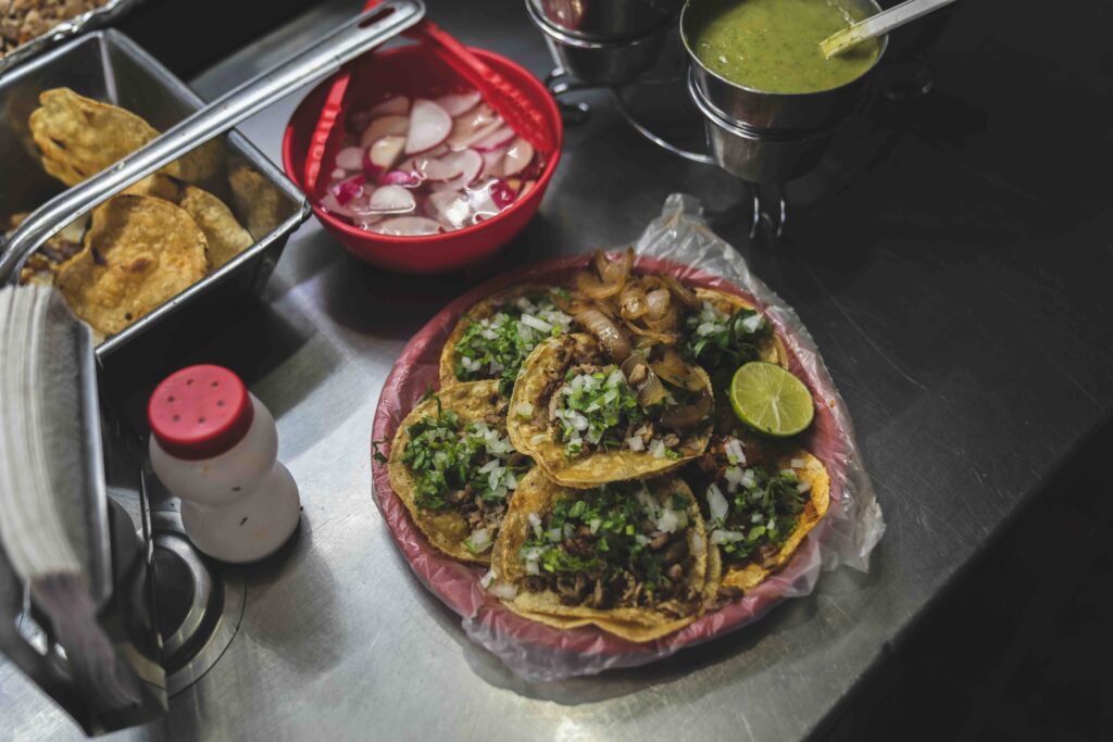 A plate of authentic tacos al pastor topped with cilantro and onions, served alongside fresh salsa and radishes. 