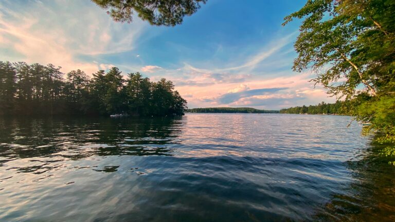 13 Best Things to Do in Freeport, Maine: Outlets, Coastal Parks & Lobster Shacks A tranquil, tree-lined lake reflecting a colorful sunset sky, representing peaceful things to do in Freeport Maine.