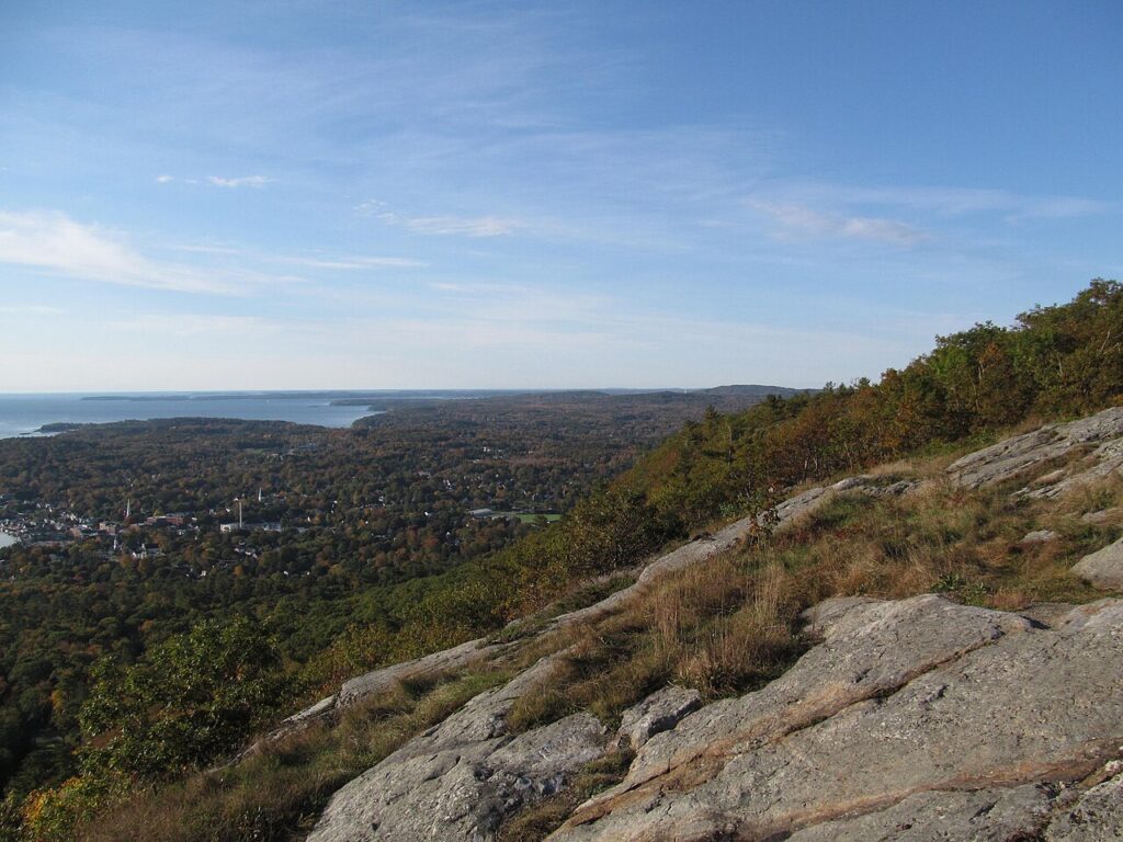 A steep, rocky granite cliff face overlooking the town and ocean from the Maiden's Cliff trail.