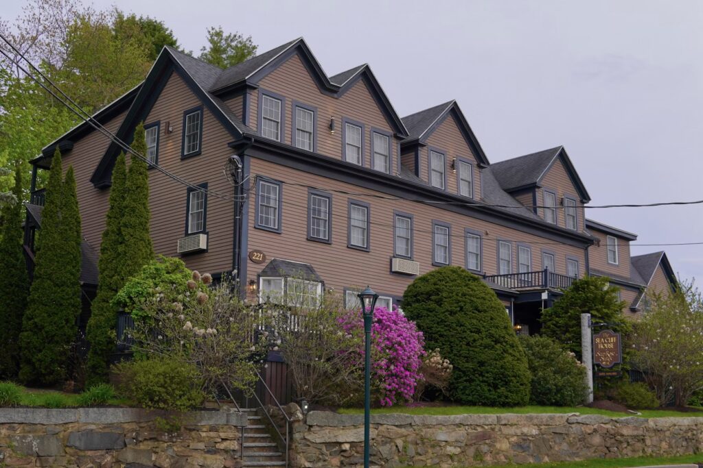A large, multi-story brown lodging building with manicured bushes located near downtown Ogunquit, Maine.