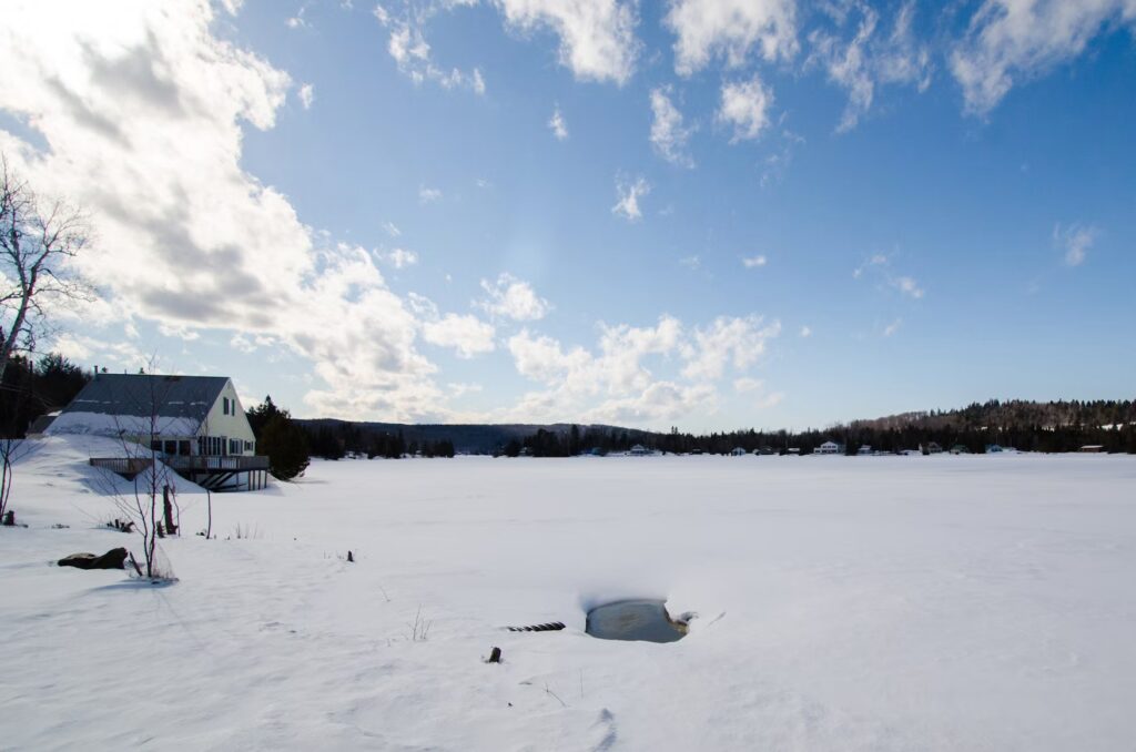 A completely frozen and snow-covered lake with a small structure on the shoreline.