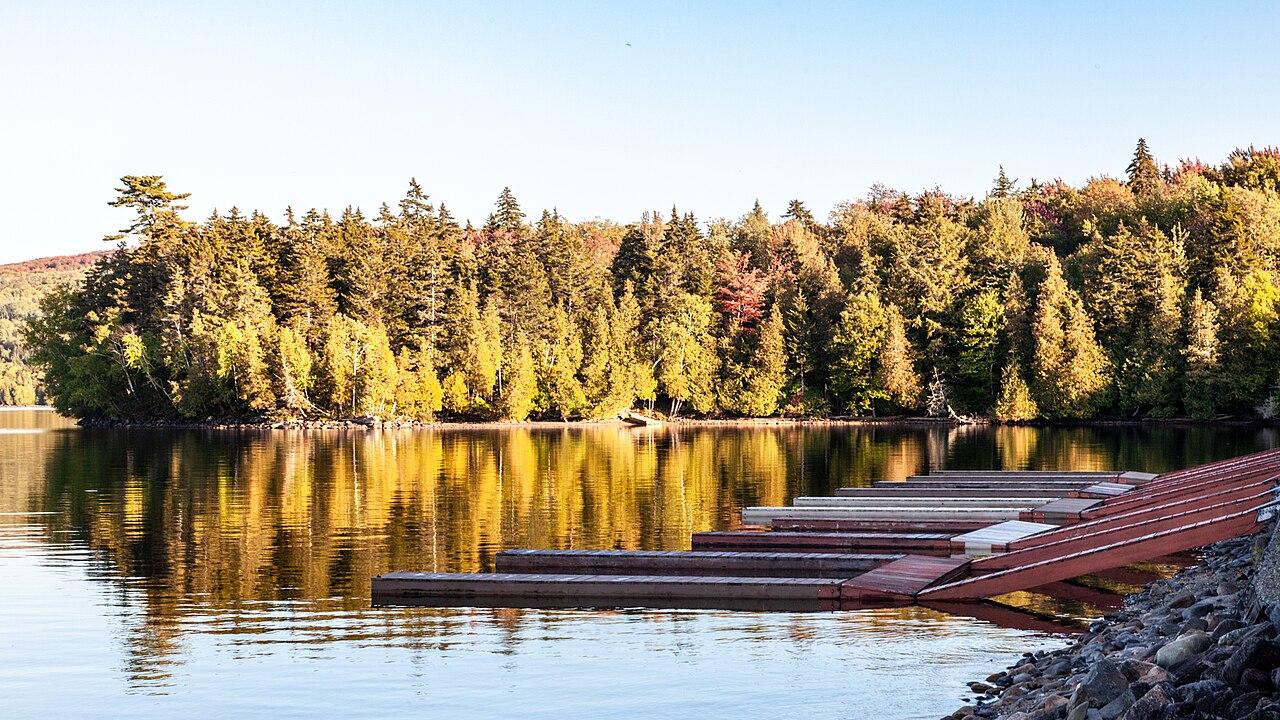 A tranquil lake reflecting golden autumn trees with wooden docks on the shore in Rangeley, Maine.