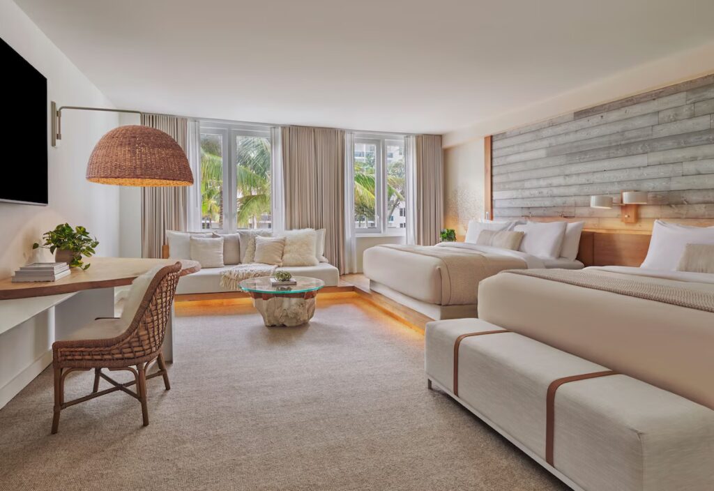 A spacious hotel room with two beds, a curved sofa, and a large round woven lamp hanging over a table.