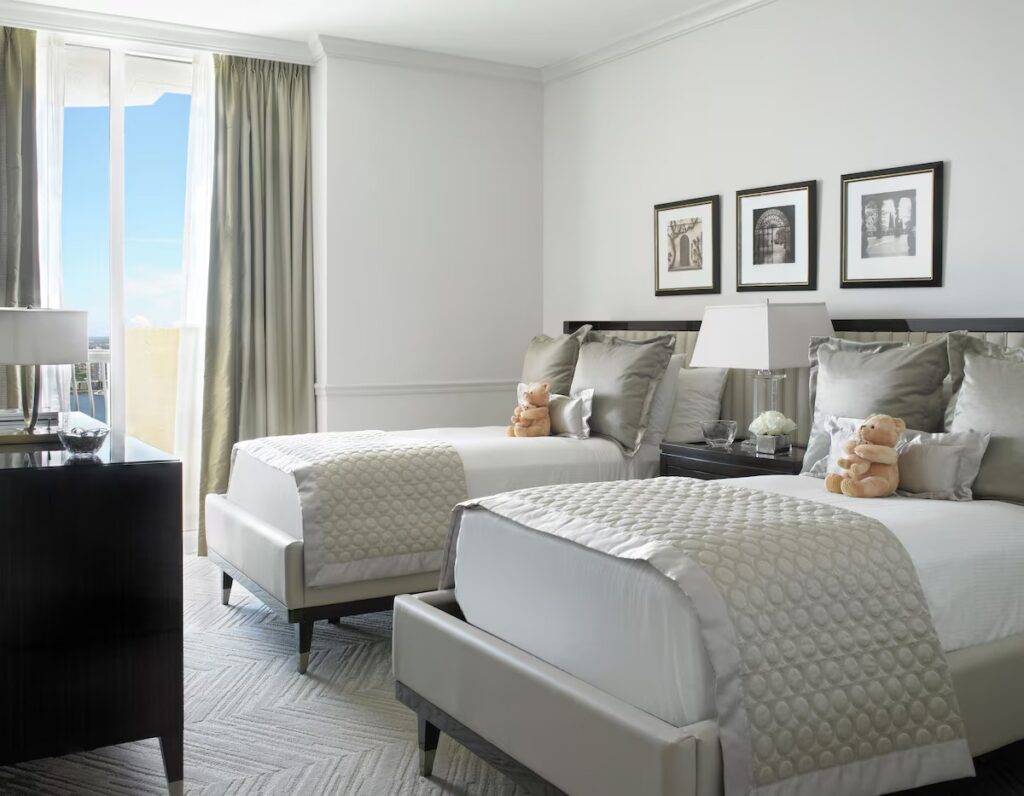 A clean white hotel room featuring two twin beds topped with stuffed teddy bears.