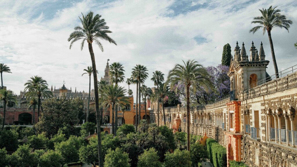 Lush gardens and tall palm trees by historic Moorish architecture in Seville.