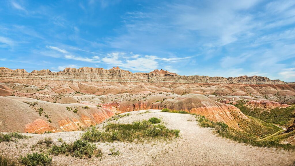 A wide view of the Badlands' colorful hills and prairie grass, featuring unique camping sites under a blue sky.