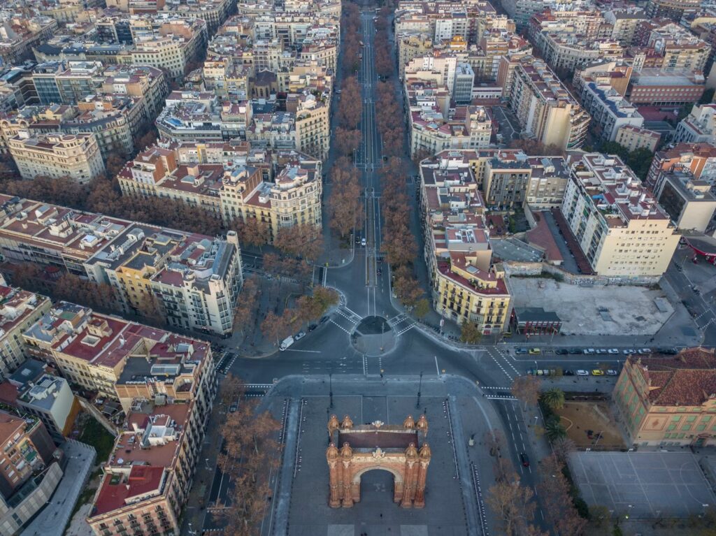 Aerial view of a tree-lined avenue leading to a red brick arch in Barcelona.