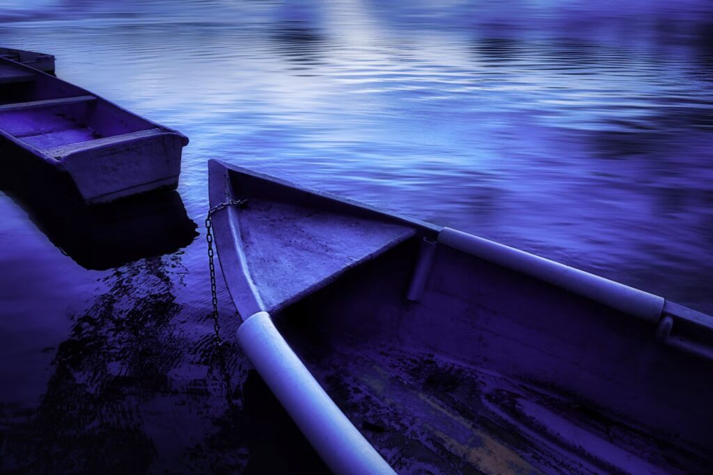 Two empty wooden boats floating on dark, still water at night.