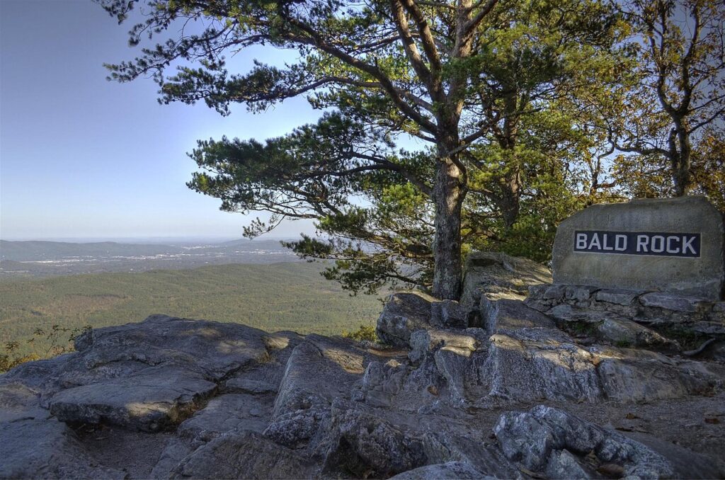 A stone marker reading "BALD ROCK" sits on a rocky overlook with a view of a sprawling green valley below.