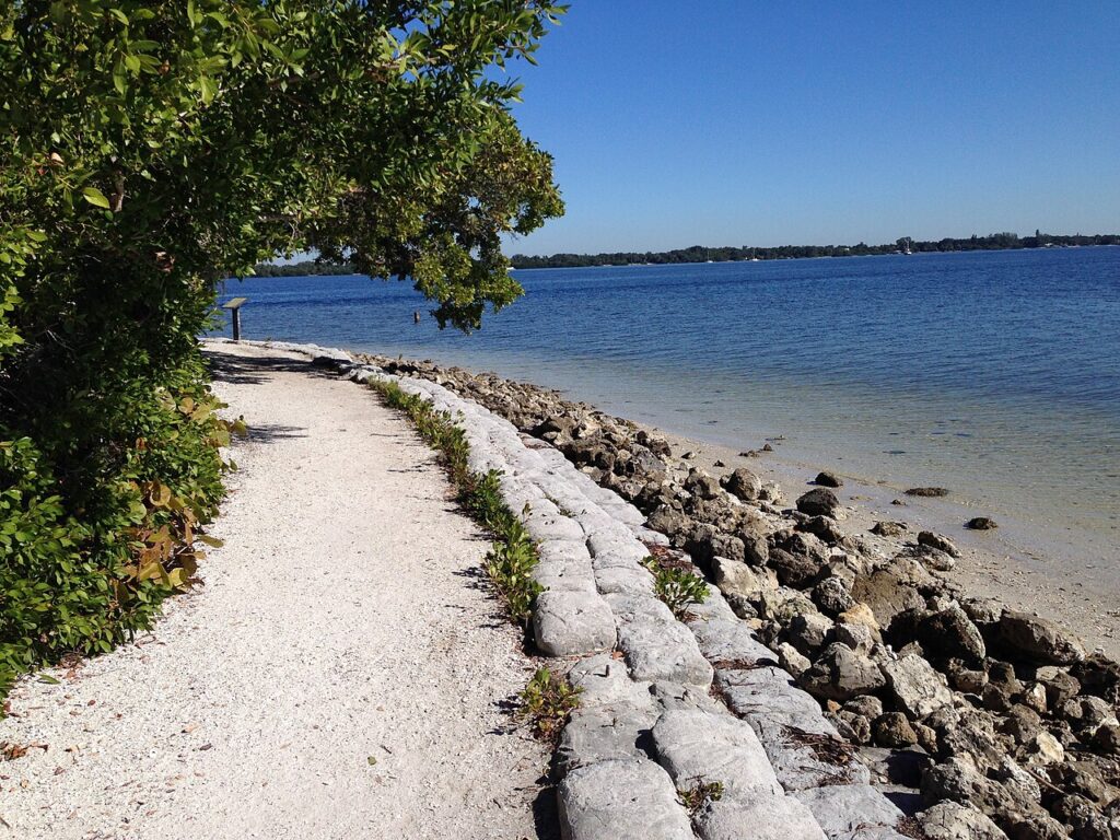 A coastal trail lined with sandbags running along the calm blue waters of De Soto National Memorial.