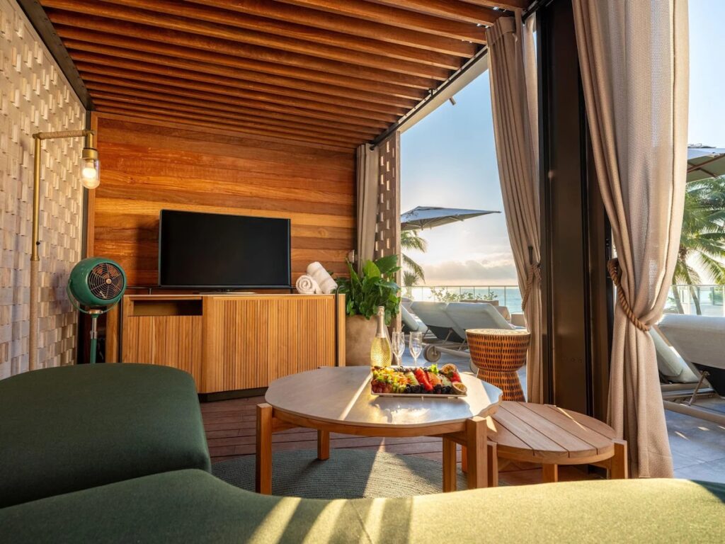 A shaded private pool cabana fitted with a couch, coffee table, TV, and ocean view.