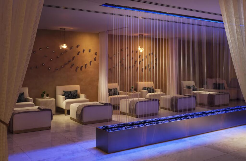 A quiet spa relaxation room with white loungers lined behind a backlit water curtain feature.