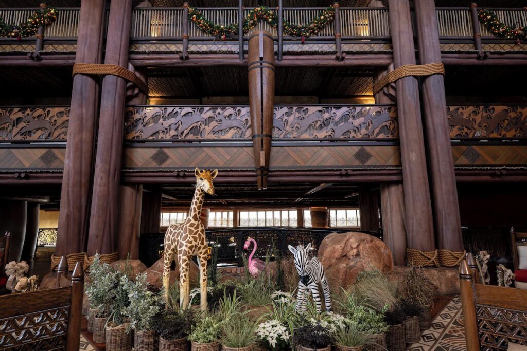 A grand wooden resort lobby decorated with life-sized statues of a giraffe, zebra, and flamingo.