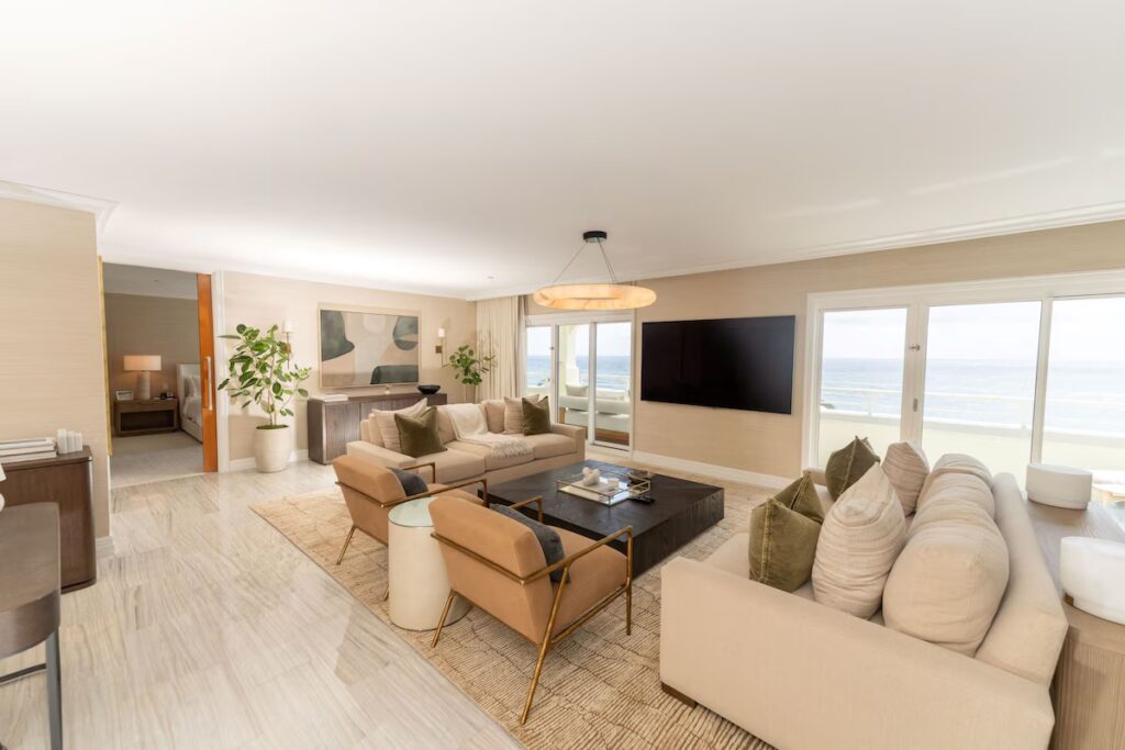 A bright and spacious living area with two large beige sofas, a modern black coffee table, and ocean views.