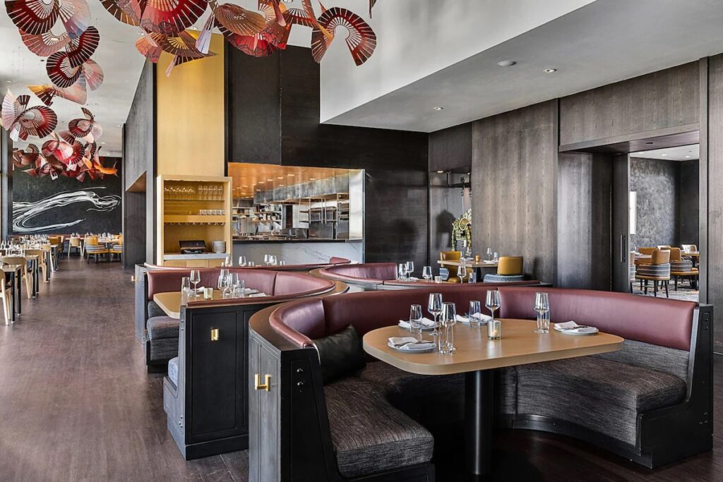 A sleek, modern restaurant interior with curved burgundy leather booths, wooden tables, and unique ceiling decorations.