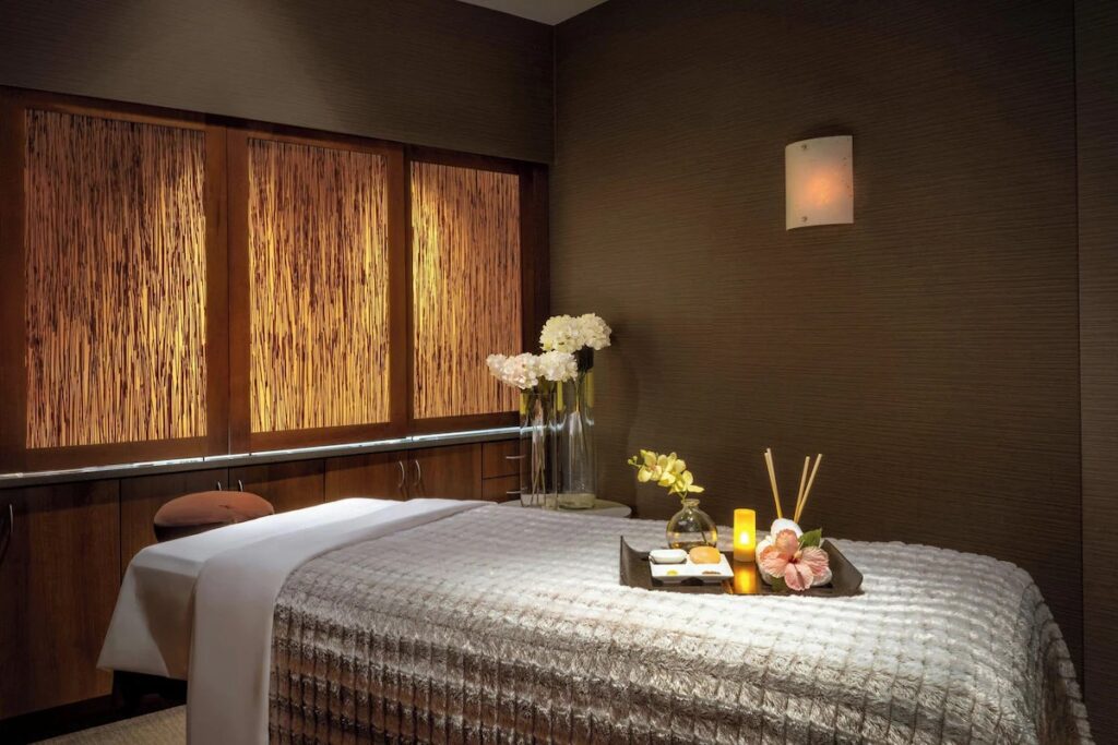 A cozy, dimly lit spa room featuring a neatly made massage table and glowing candles.