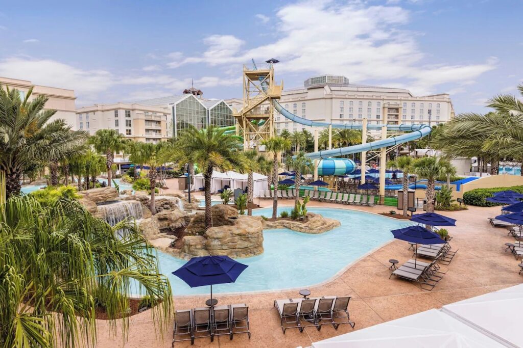 High-angle view of an expansive resort pool area with waterfalls, palm trees, and a slide tower.
