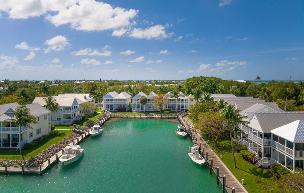 An aerial view of pastel resort villas lining a calm green water canal with docked boats.