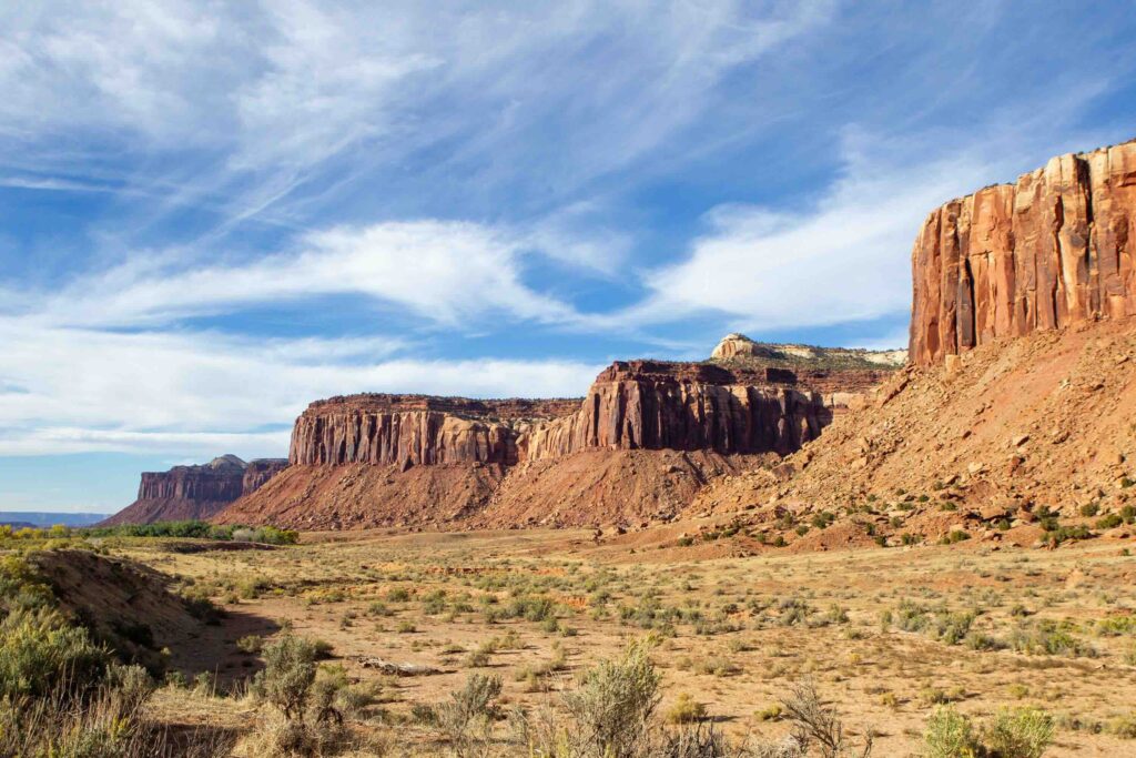 A panoramic view of flat desert terrain leading up to a line of towering, flat-topped red sandstone mesas.