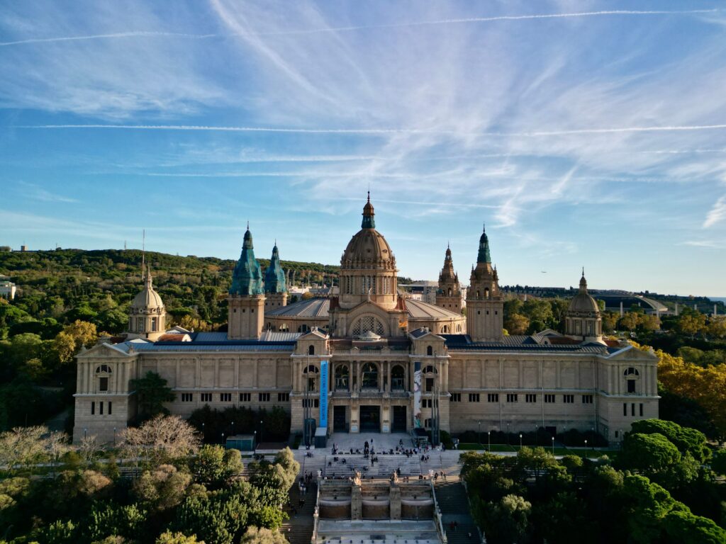 The grand, domed Palau Nacional building viewed from a high angle, with clear blue skies above.
