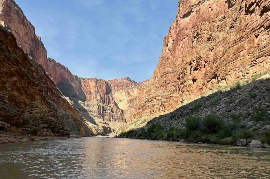 The Paria River flows smoothly through a deep, narrow canyon flanked by towering red sandstone walls.