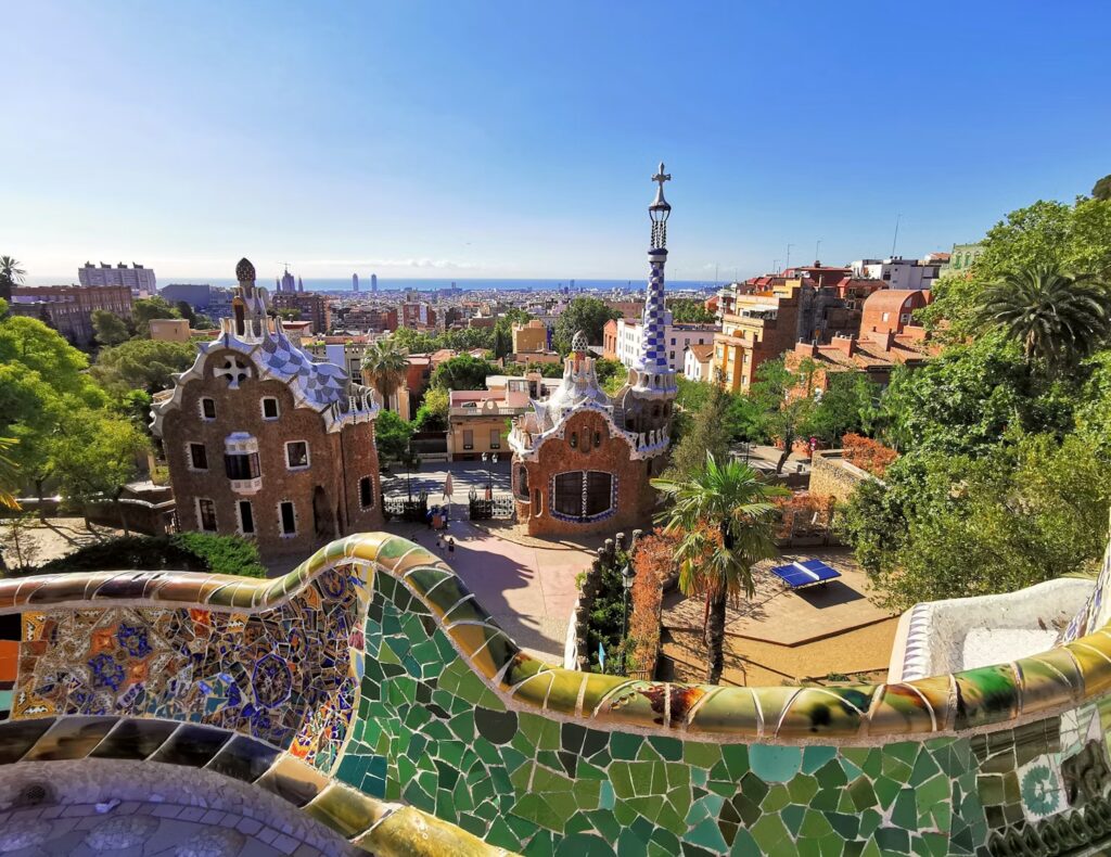 A colorful, mosaic-tiled bench overlooking the whimsical architecture and greenery of Park Güell.