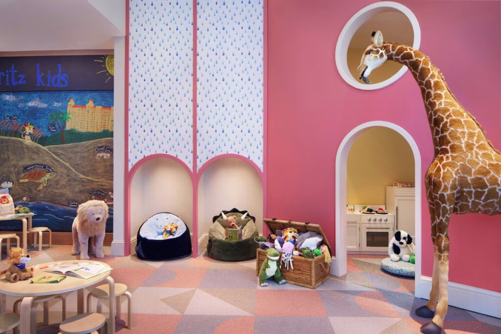 A vibrant kids' play area featuring a pink giraffe statue, beanbags, and a chalkboard wall.