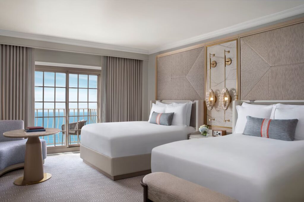 An elegant hotel bedroom with two queen beds, sophisticated decor, and an oceanfront balcony.
