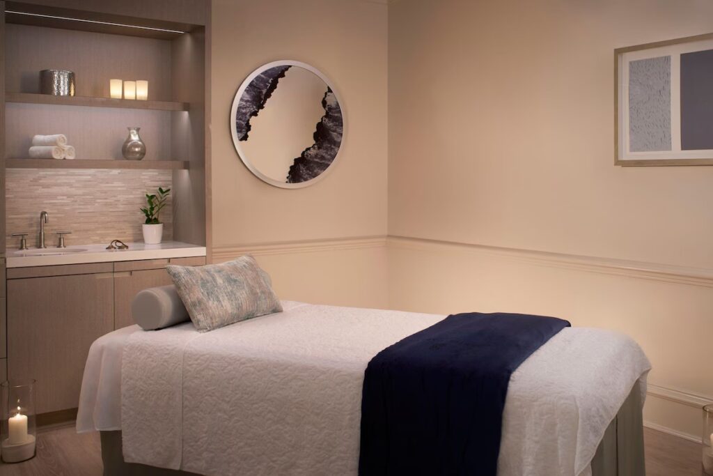 A peaceful spa treatment room with a single massage bed, neutral decor, and soft lighting.