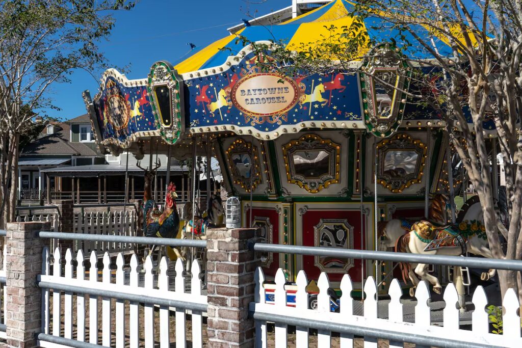 A colorful outdoor carousel with carved horses surrounded by a white picket fence.