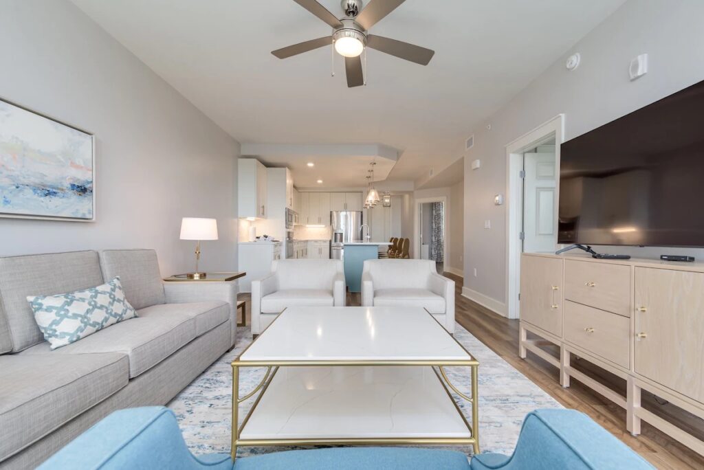 A modern condo living room featuring a grey sofa, light blue armchairs, and an open kitchen.