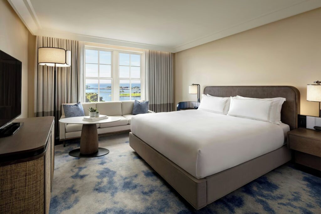 A modern bedroom at The Vinoy Resort featuring a king bed, grey sofa, and a blue and white patterned rug.