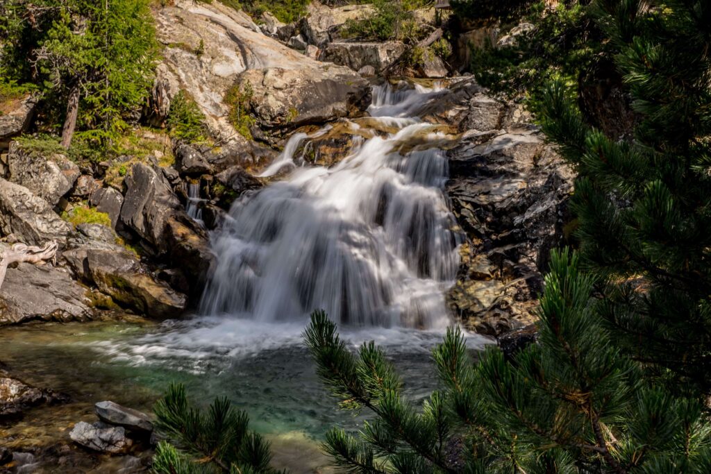 Waterfall cascading over dark rocks in pine forest at sierra nevada camping locations.