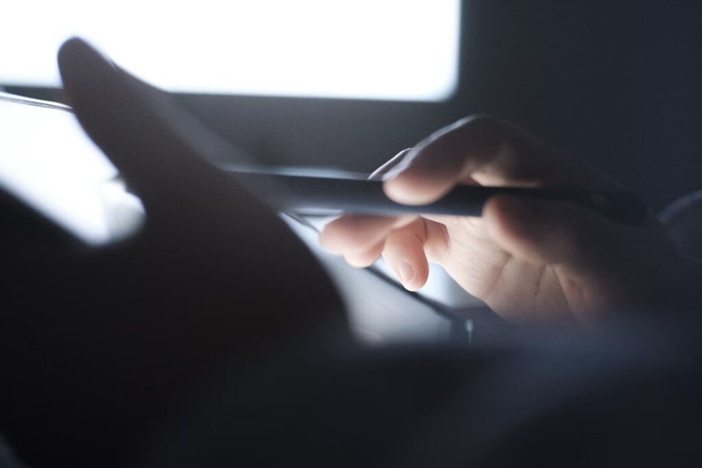 A close-up of a passenger's hand using a stylus to navigate a tablet screen during a flight.